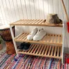 A shoe rack with shoes and a hat on it, placed on a colorful rug in front of a white slatted wall. Podgląd zdjęcia produktu