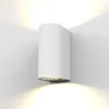 A white cylindrical outdoor wall light mounted on a white wall, casting warm light upwards and downwards. Produktbild-Vorschau