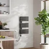 A modern bathroom or kitchen setting with a dark grey towel warmer mounted on a textured wall, next to a large potted plant and a wooden cabinet. Náhľad obrázku produktu