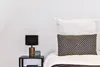 A close-up view of a bedside table with a lamp and a digital alarm clock next to a bed with pillows. Anteprima dell’immagine prodotto