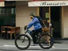 A man rides an electric bicycle past a brasserie. Produktbild-Vorschau