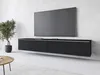 A modern black TV stand mounted on a textured concrete wall, with a large flat-screen TV on top. A potted plant is to the left, and a round wooden coffee table is in the foreground. Anteprima dell’immagine prodotto