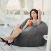 A woman sits on a large beanbag chair outdoors, holding a drink. Náhled obrázku produktu