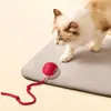 A cat is playing with a red interactive toy on a gray mat. Náhled obrázku produktu