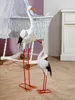 Two decorative storks are placed next to a baby bassinet in a nursery setting. Anteprima dell’immagine prodotto