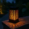 A solar lantern with a flame effect sits on a stone surface at dusk, casting patterned light. Podgląd zdjęcia produktu