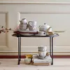 A collection of ceramic cups and saucers, a teapot, and some cookies are arranged on a small table. Produktbild-Vorschau