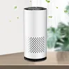 A white cylindrical air purifier sits on a wooden table, with blurred green plants and windows in the background. Small green leaf graphics and bubbles float around the air purifier. Produktbild-Vorschau