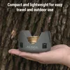A hand holding a small camping stove against a tree bark background. Produktbild-Vorschau