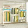 A white metal garment rack with shelves, filled with clothes on hangers and some boxes. Podgląd zdjęcia produktu
