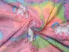 A close-up view of a soft, fuzzy blanket with a rainbow stripe pattern and unicorn prints. Anteprima dell’immagine prodotto