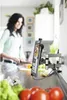 A woman is cooking in a kitchen while a tablet is mounted on the wall with a recipe displayed. Podgląd zdjęcia produktu
