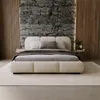 A modern bedroom with a large upholstered bed as the focal point, set against a textured stone wall and wooden paneling. Produktbild-Vorschau