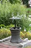 A wicker table with a built-in cooler and wine glasses on top, set in a garden next to a body of water. Produktbild-Vorschau