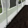 A close-up view of the lower section of a white transparent greenhouse with metal poles, showing the base secured to the ground with ties. Produktbild-Vorschau