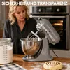 A woman is in a kitchen with a stand mixer, a jar of flour, and a cinnamon roll. Produktbild-Vorschau