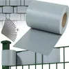 A roll of grey privacy screen material is shown unrolling over a green wire fence. Several grey clips and a green fence post are also visible. Náhled obrázku produktu