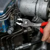 A person's hand is using KNIPEX TwinGrip pliers to work on a complex mechanical assembly with many tubes and fittings. Voir les images du produit