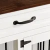 A close-up view of a white dog crate with black hardware, showing a drawer handle and a hinge on a door. Produktbild-Vorschau