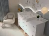 A nursery room with a changing table, a chair, and a lamp. Podgląd zdjęcia produktu