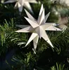 A white origami star ornament is placed on a green Christmas tree branch. Produktbild-Vorschau
