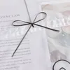 A close-up of a white fabric with text and a dark ribbon tied in a bow. Produktbild-Vorschau