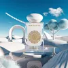 A perfume bottle is displayed in a surreal, desert-like environment with abstract white structures and fluffy trees. Anteprima dell’immagine prodotto