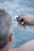 A person's hand holding a remote control over a bubbling hot tub. Produktbild-Vorschau