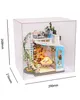 A miniature dollhouse with furniture and accessories inside a clear display box, with dimensions indicated. Náhľad obrázku produktu