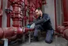 A man is working on red pipes in a mechanical room. Produktbild-Vorschau