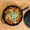 A cast iron skillet filled with food, including chicken, vegetables, and garnishes, sits on a wooden surface. Voir les images du produit
