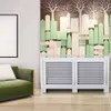 A white radiator cover is shown in a room with a green sofa and a decorative wall panel. Náhľad obrázku produktu
