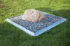A rock sits on a bed of gravel within a metal frame on a lawn. Produktbild-Vorschau