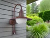 A split image showing an outdoor wall light on the left and a lush garden on the right. Produktbild-Vorschau