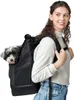 A woman is wearing a black backpack with a small dog inside, against a white background. Produktbild-Vorschau