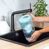 A person is rinsing a water filter pitcher under a faucet in a kitchen sink. Náhľad obrázku produktu