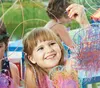 Three young girls are drawing with colorful chalks on a glass surface outdoors. Voir les images du produit