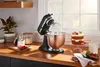 A black KitchenAid stand mixer with a copper bowl is shown on a wooden countertop next to a small cake and a jar of milk. Podgląd zdjęcia produktu