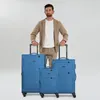 A man stands behind three blue suitcases of varying sizes. Voir les images du produit