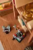 LEGO® building blocks are arranged on a wooden surface, with books and a glass jar in the background. Produktbild-Vorschau