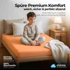 A young boy sitting cross-legged on a bed with an orange fitted sheet, pillows, and a blanket. Náhľad obrázku produktu