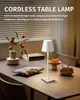 A cordless table lamp is shown on a wooden table, with some decorative items and snacks. Produktbild-Vorschau