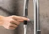 A hand is shown pressing a button on a faucet sprayer, with water flowing out. Produktbild-Vorschau