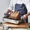 A person in an apron is holding a roasting pan with a large roast beef inside, placed on a wooden cutting board. Produktbild-Vorschau
