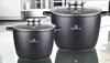 Two black pots with speckled coating and glass lids are displayed on a reflective surface in a kitchen setting. Produktbild-Vorschau