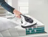 A person is using a handheld vacuum cleaner on a mattress. Produktbild-Vorschau