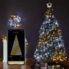 A decorated Christmas tree with lights, a wreath, and a smartphone displaying a lighting pattern. Produktbild-Vorschau