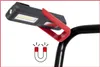 A close-up of a black and red workshop hand lamp attached to a black metal bar, with a magnetic symbol shown below. Podgląd zdjęcia produktu