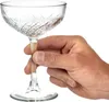 A hand holding a clear glass champagne coupe. Produktbild-Vorschau
