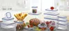 A collection of clear plastic food storage containers with blue lids, some filled with food items like pasta, nuts, and vegetables, arranged on a surface in a kitchen-like setting. Anteprima dell’immagine prodotto